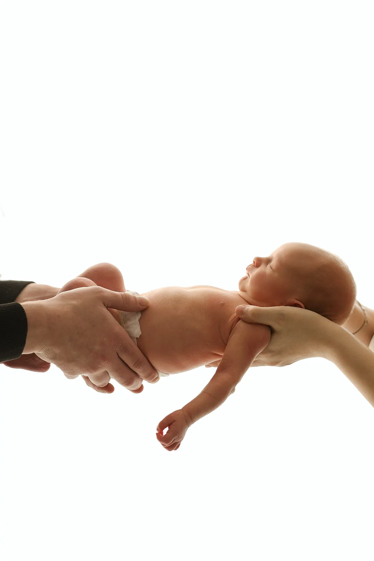 Newborn lifted between mother's and father's hands, back-lit