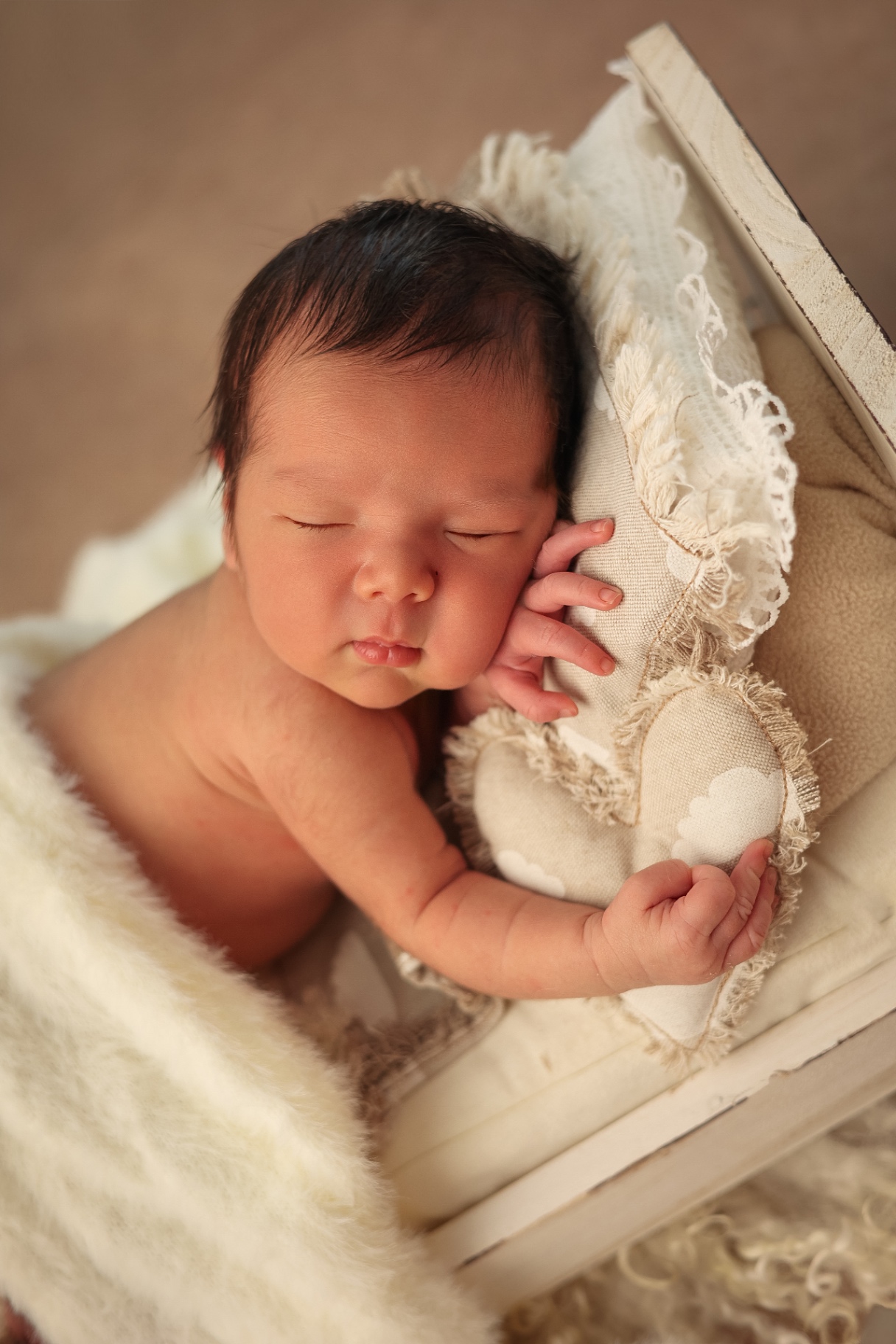 Sleeping newborn holding a linen heart pillow in a little white bed