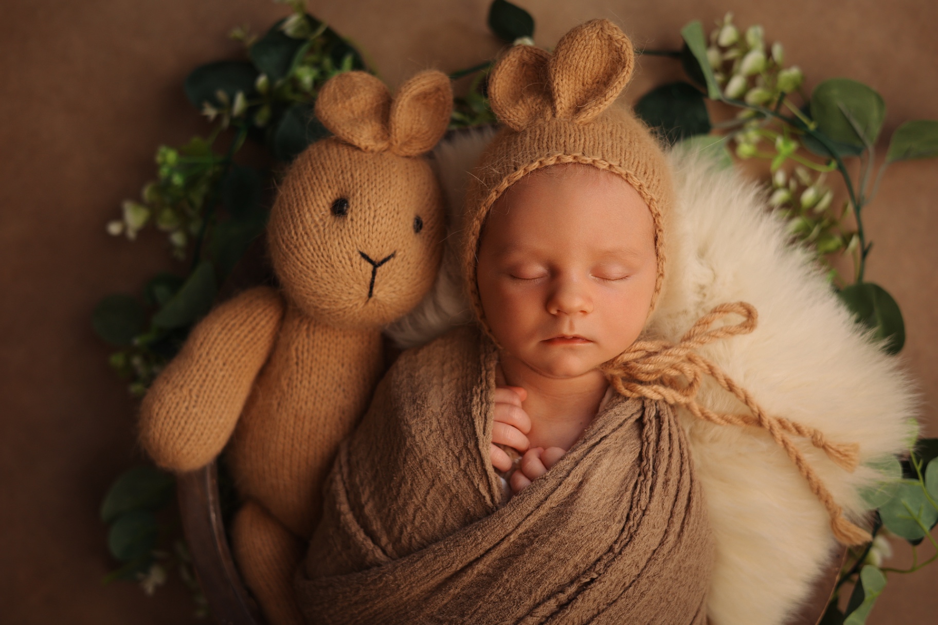 Newborn photography Colindale — Newborn in a bunny-ear bonnet asleep beside a knitted bunny toy and eucalyptus