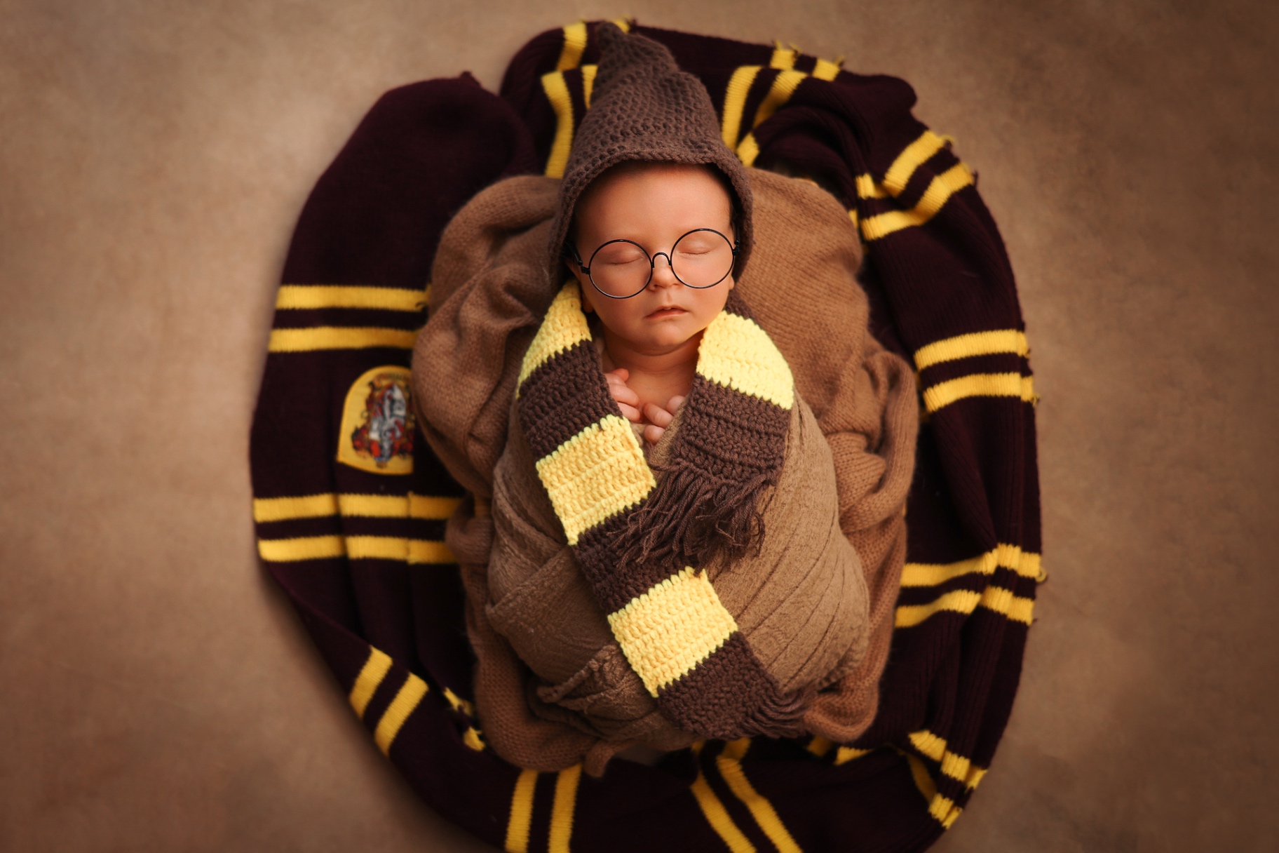Newborn dressed as a little wizard with round glasses and a striped scarf