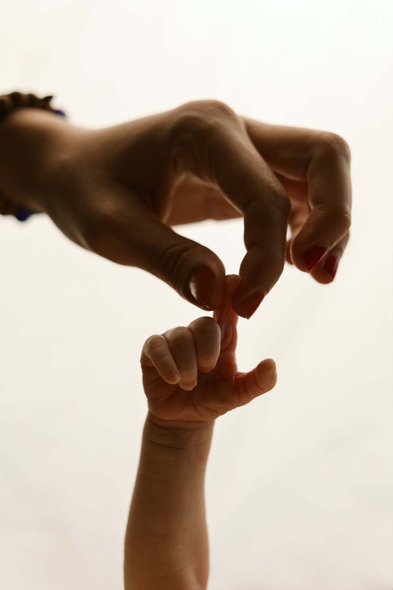 Newborn hand holding mother's finger against a warm cream background