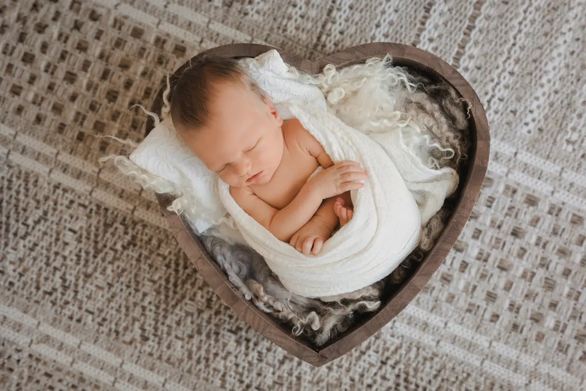 Sleeping newborn wrapped in white fabric inside a heart-shaped basket