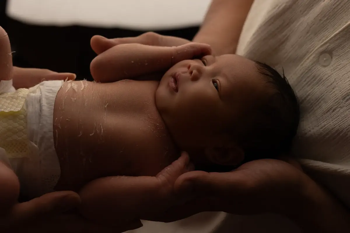 Newborn cradled in parents' hands in warm, moody light