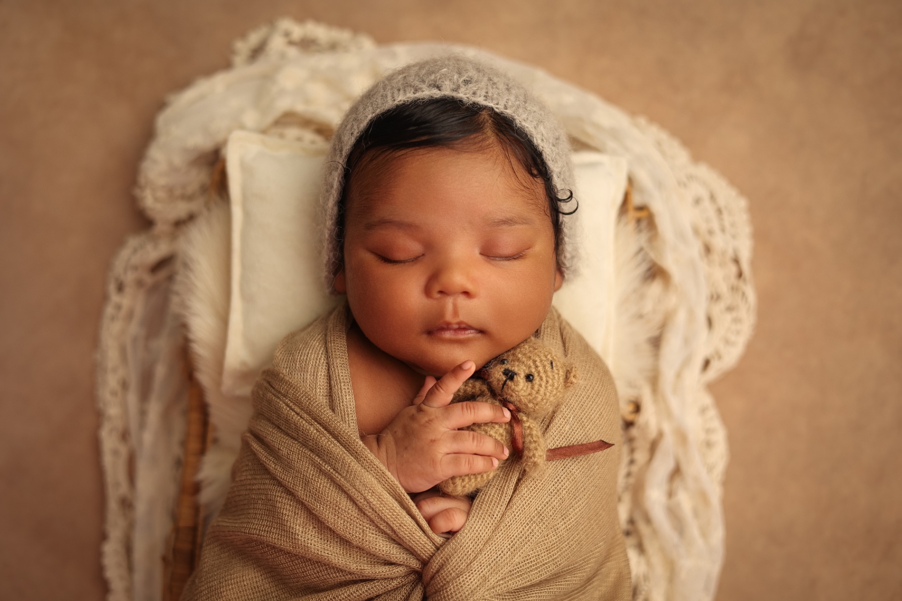 Newborn photography Colindale — Newborn in a grey knit bonnet cuddling a tiny teddy bear in a basket