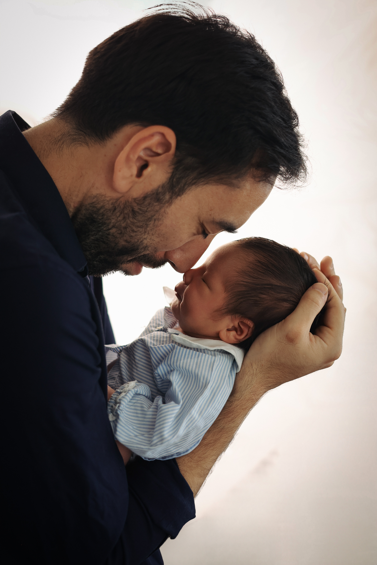 Newborn photography Colindale — Father touching foreheads with his newborn baby in soft backlight