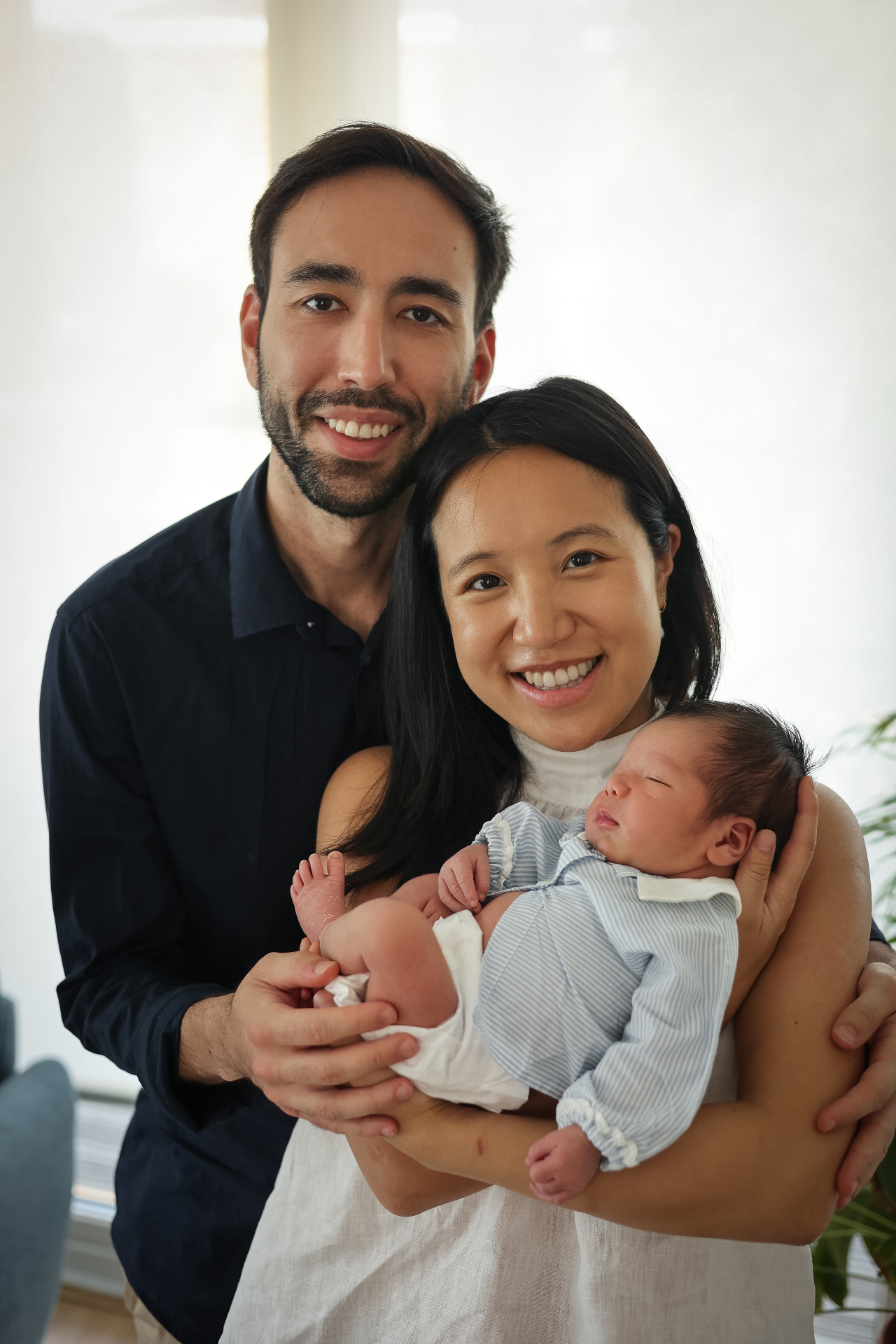 Smiling parents holding their newborn baby in soft window light