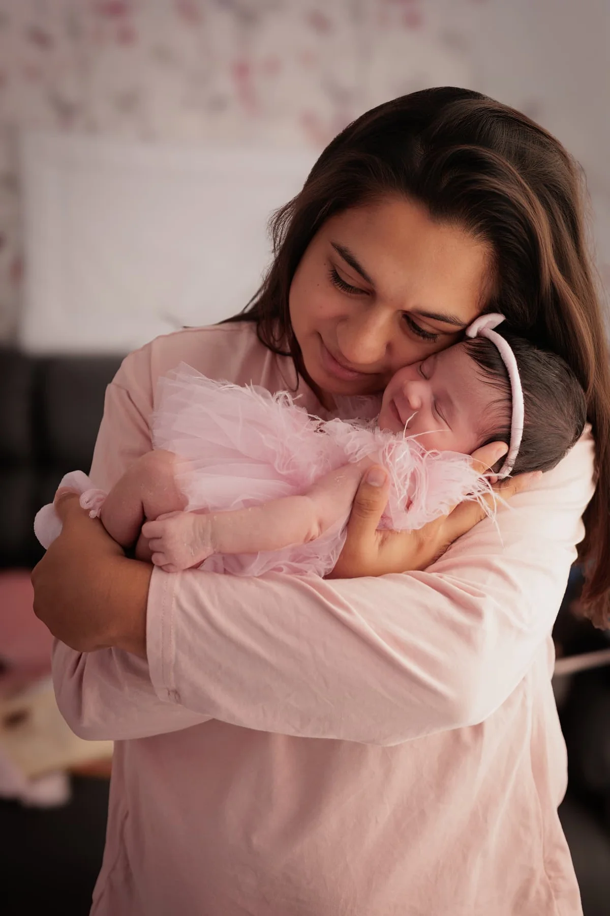 Mother cuddling her sleeping newborn girl dressed in a pink tutu with a bow headband — photographed in a Mill Hill garden room