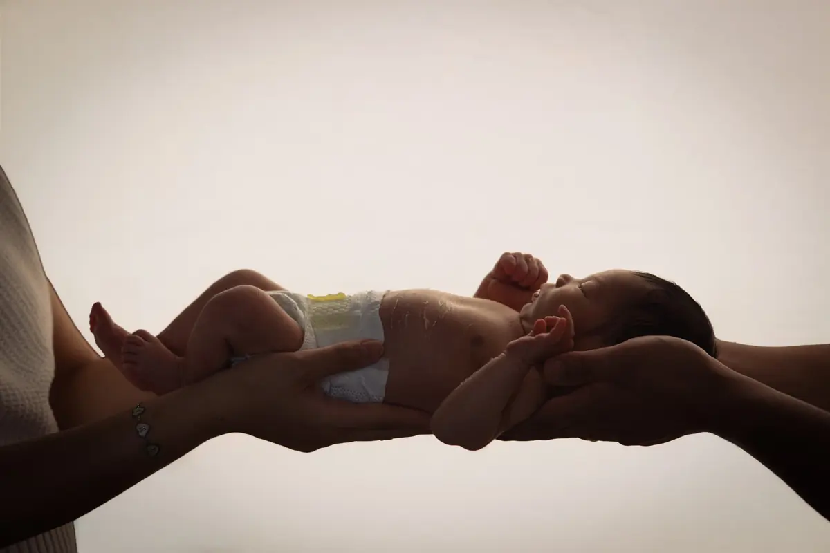 Newborn held between parents' hands in a soft backlit silhouette portrait