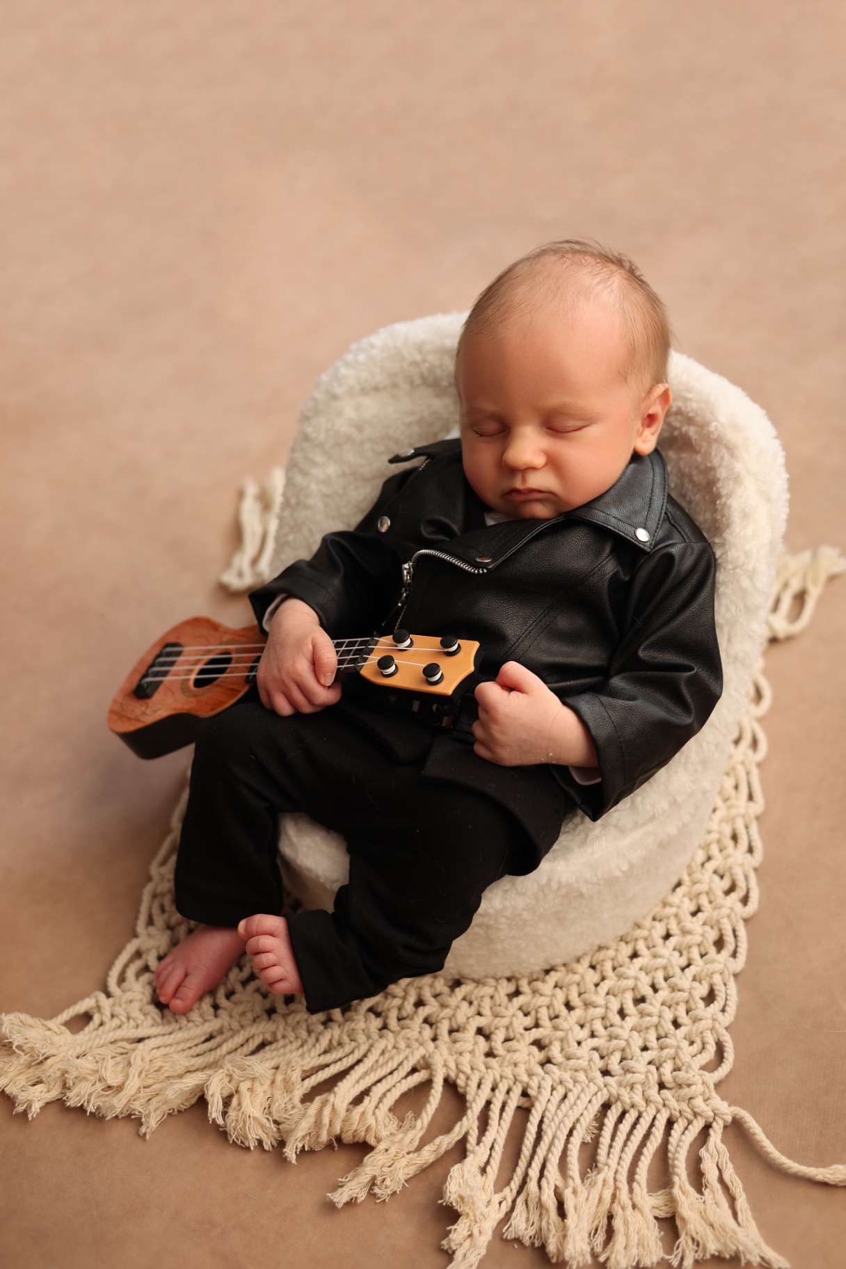 Newborn in a black leather jacket asleep with a tiny ukulele