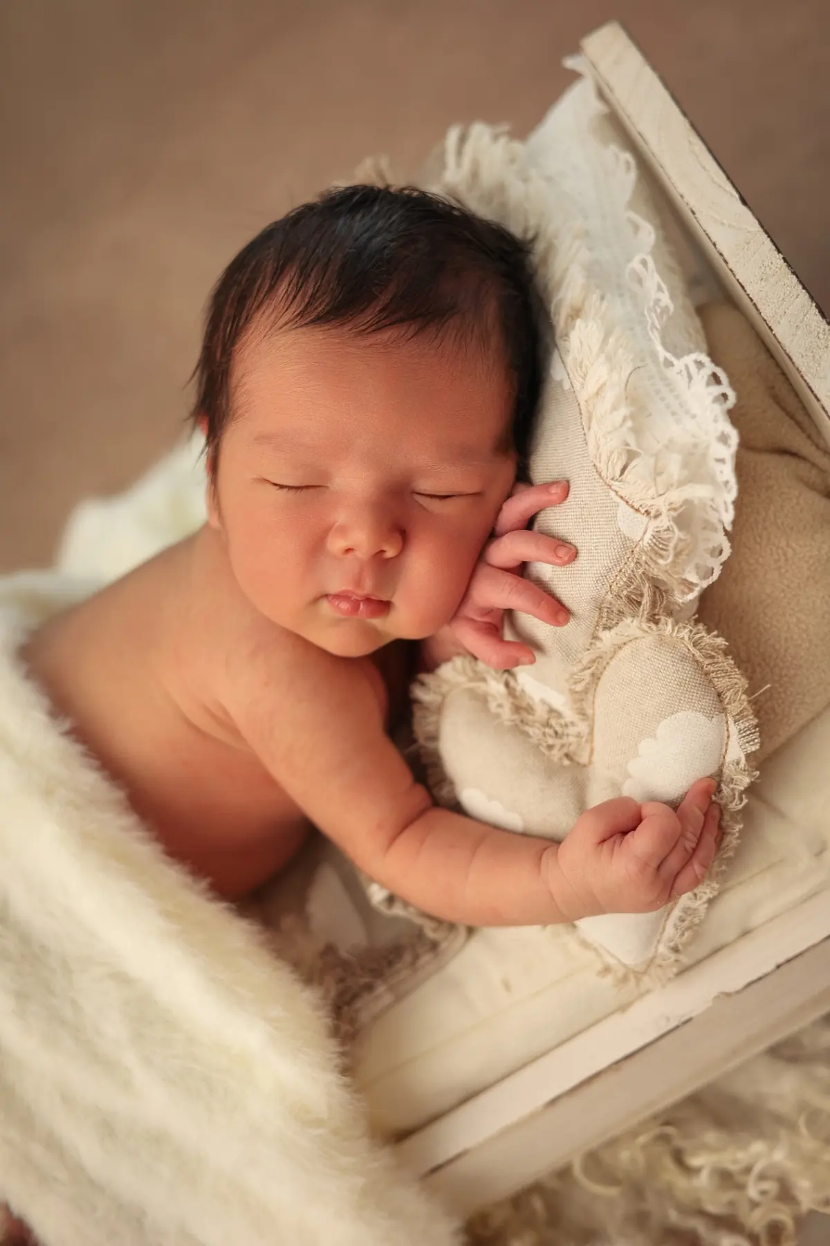 Sleeping newborn holding a linen heart pillow in a little white bed