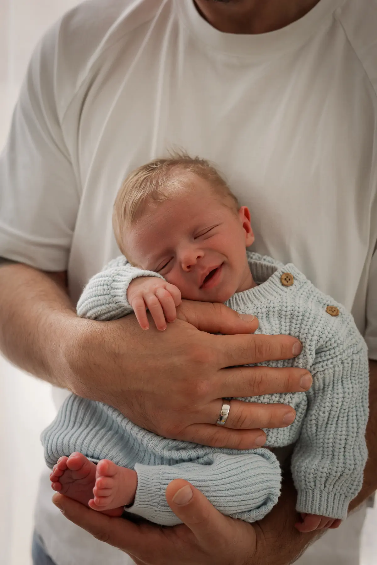 Smiling newborn in father's arms wearing a soft knit outfit