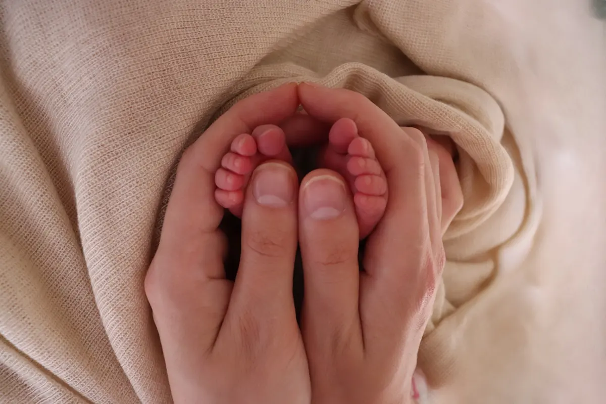 Newborn feet held in palms wrapped in soft blush fabric