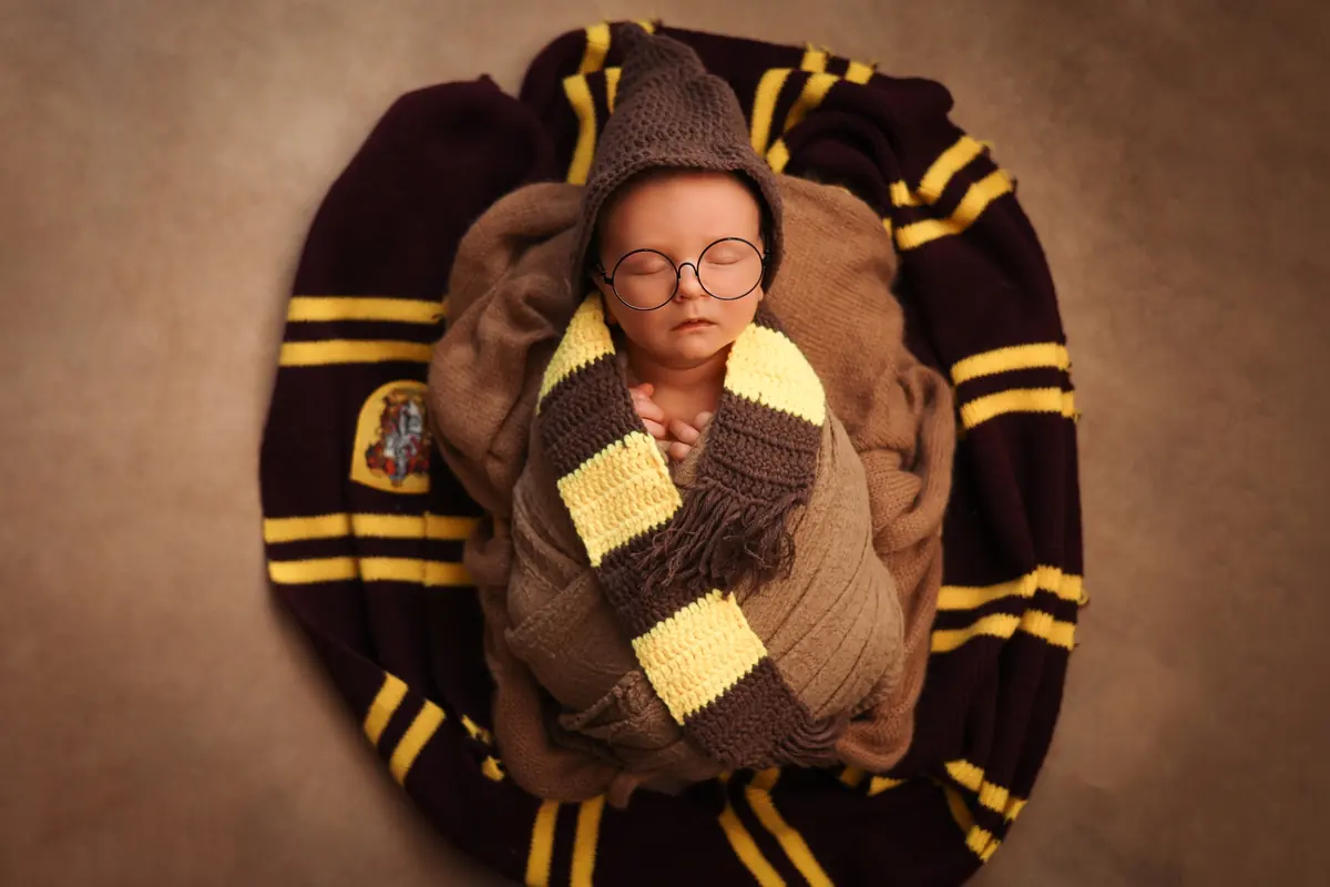 Newborn dressed as a little wizard with round glasses and a striped scarf