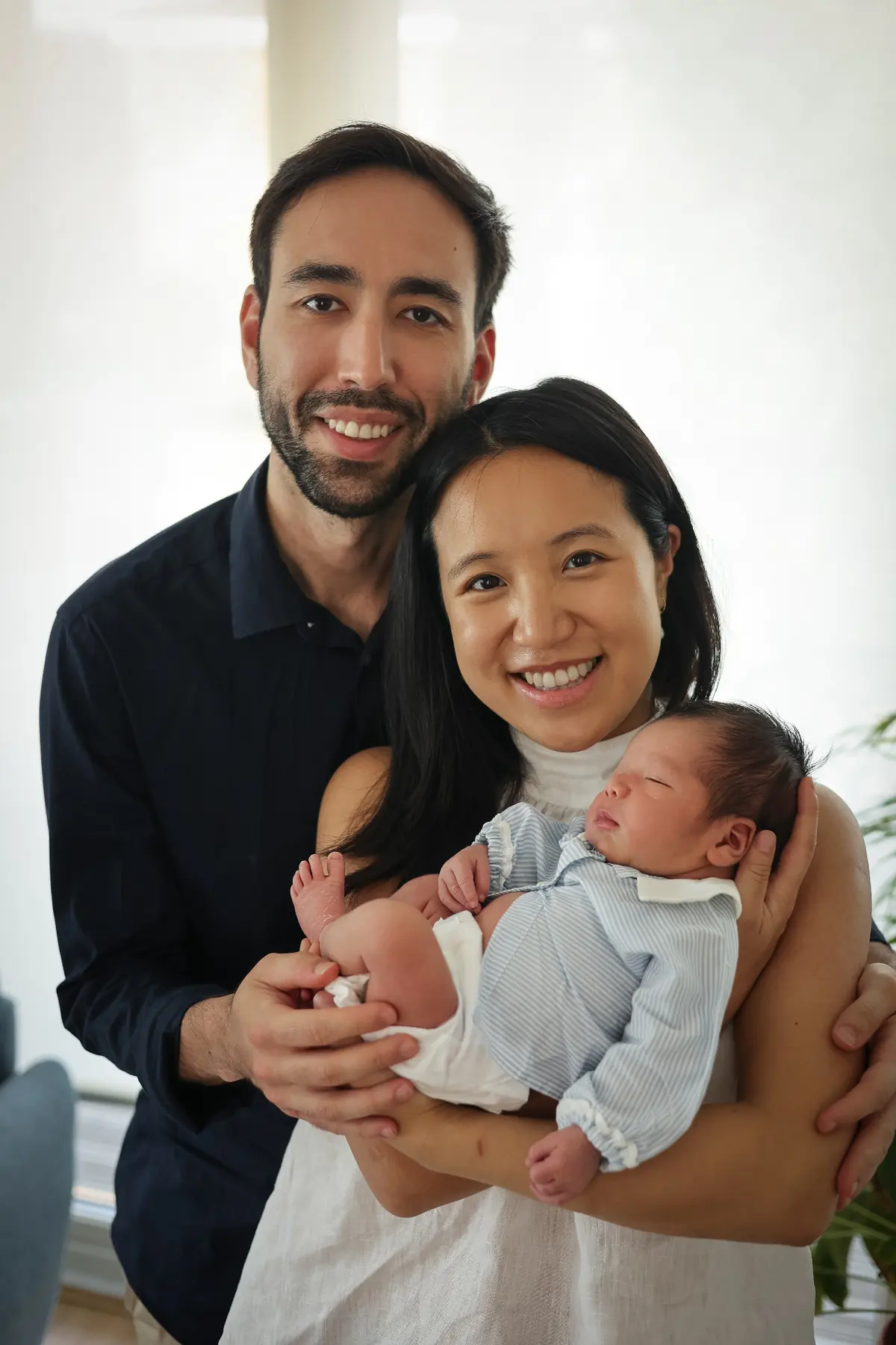 Smiling parents holding their newborn baby in soft window light