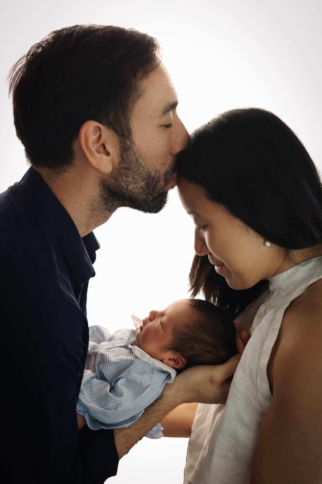 Father kissing mother's forehead as she holds their newborn baby