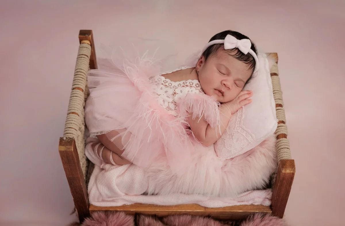 Newborn in a pink tutu and bow asleep in a little wooden bed on white bedding — in an East Finchley family home, N2