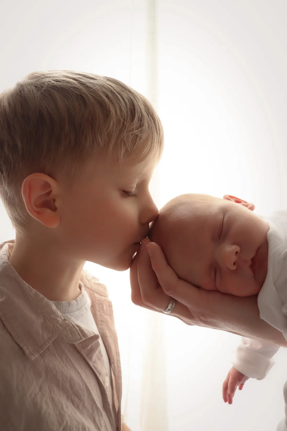 Older sibling kissing a sleeping newborn on the forehead
