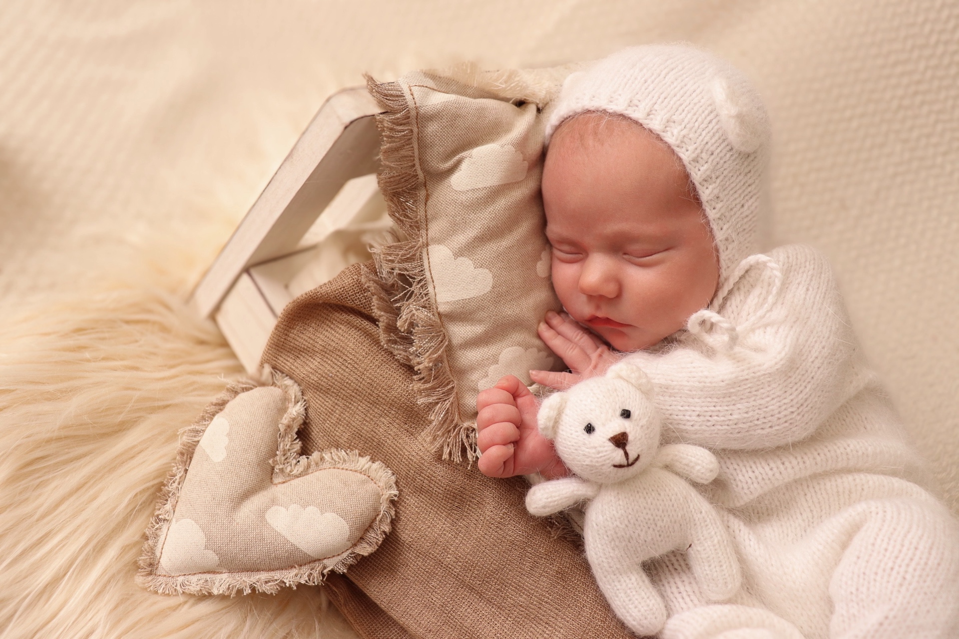 Sleeping newborn in white knit with a small teddy bear