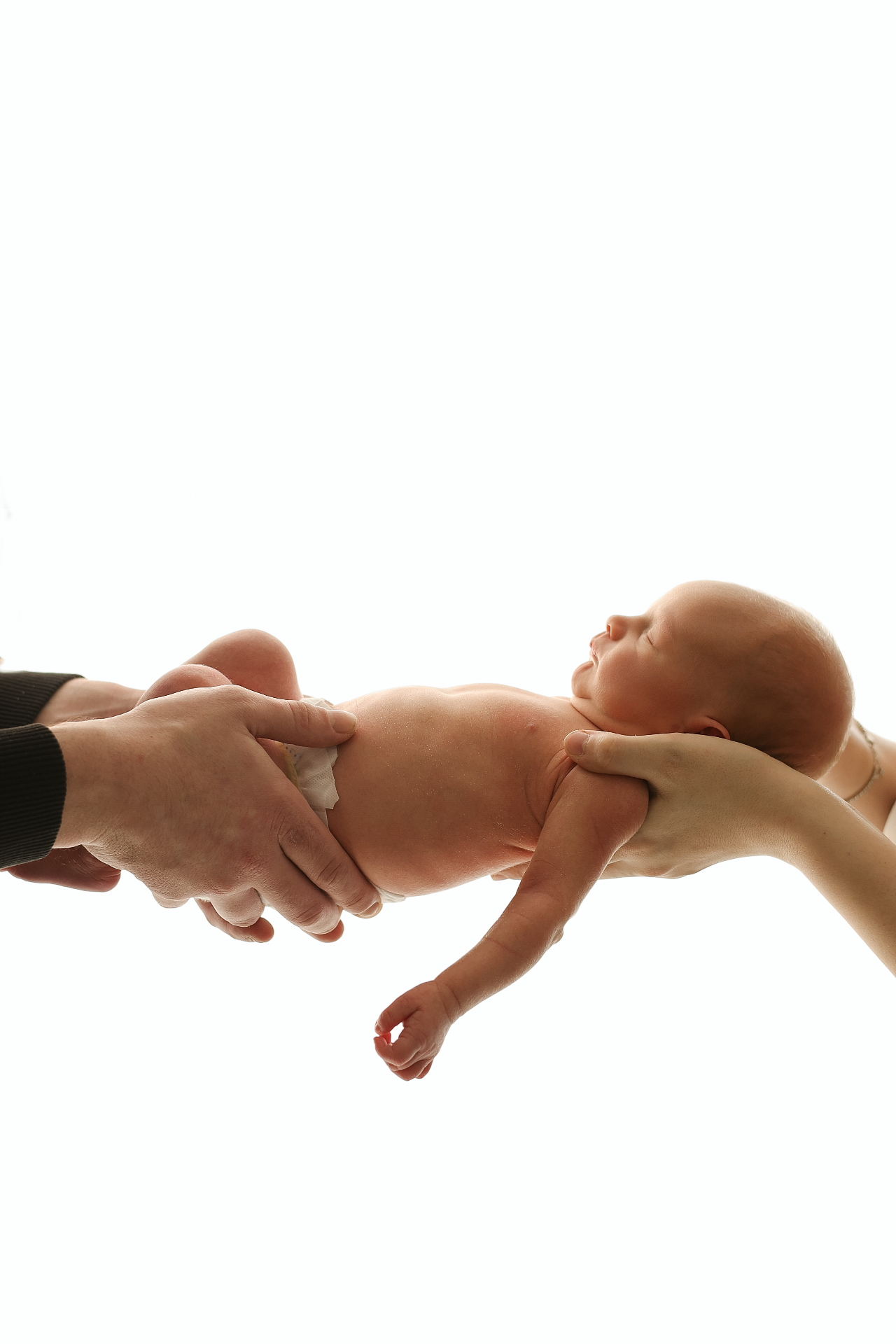 Newborn lifted between mother's and father's hands, back-lit