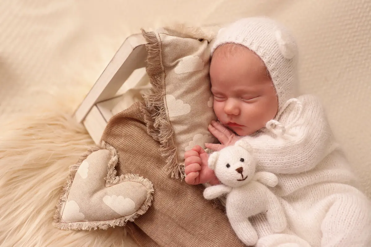 Sleeping newborn in white knit with a small teddy bear